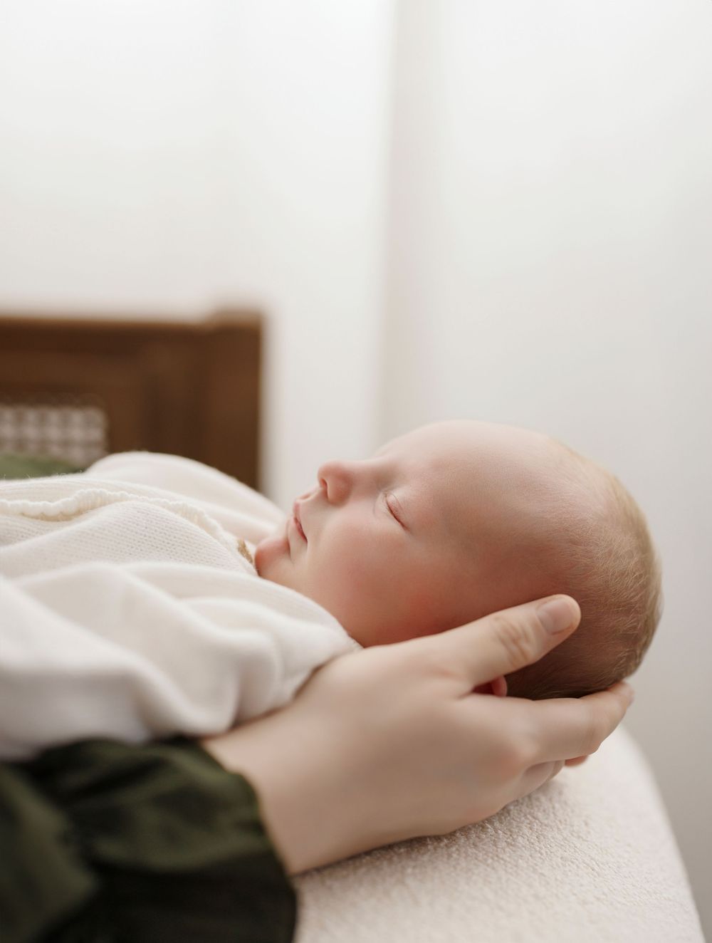 A newborn baby sleeping peacefully while a parent gently cradles their head in soft hands.