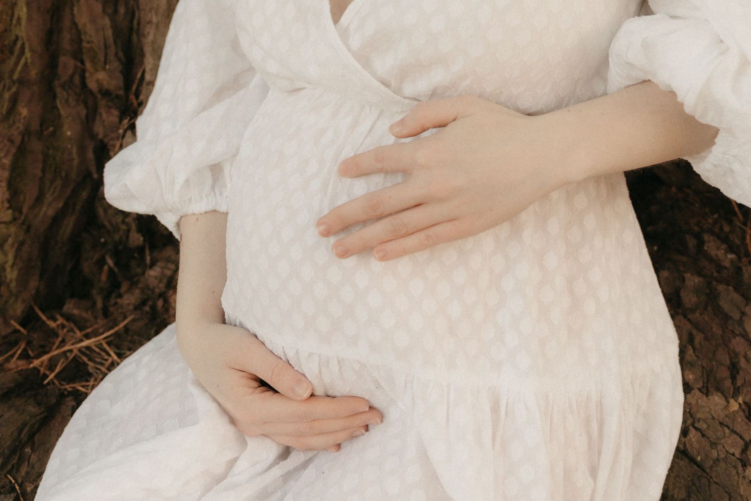 Close-up of tiny newborn baby feet peeking out from a soft cream knit blanket on a floral muslin surface.