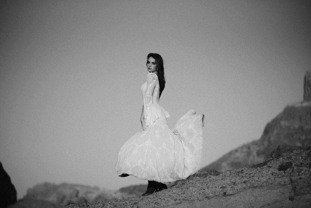 Black and white photo of a woman in flowing white gown twirling in a rocky desert landscape.