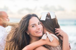 Young woman with long brown hair smiling while sharing a warm embrace on a beach.
