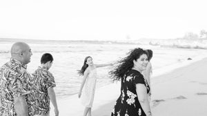 Black and white candid photo of family walking along ocean shoreline on a breezy day.