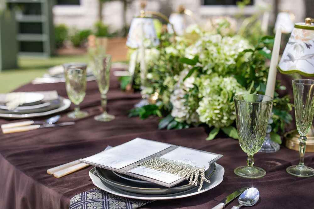 Elegant wedding table setting with green floral centerpiece, crystal glasses, and dark purple linen tablecloth.