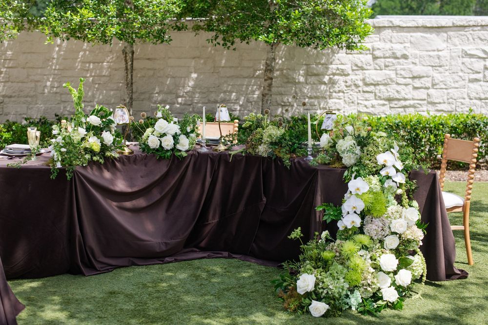 Elegant outdoor wedding reception table with dark purple linen and lush white and green floral arrangements.