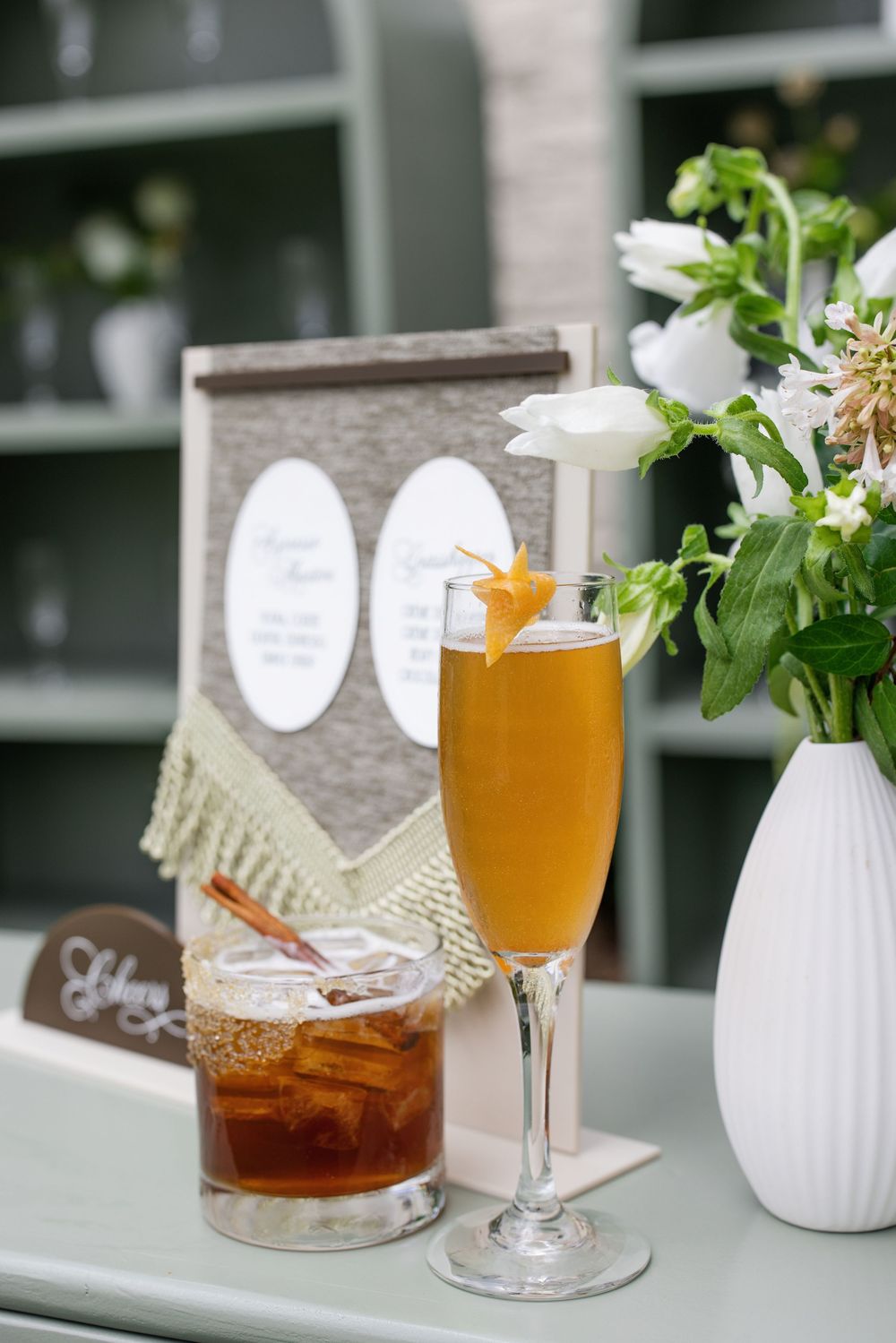 Two elegant cocktails on a table with white flowers and a menu card at a wedding reception.