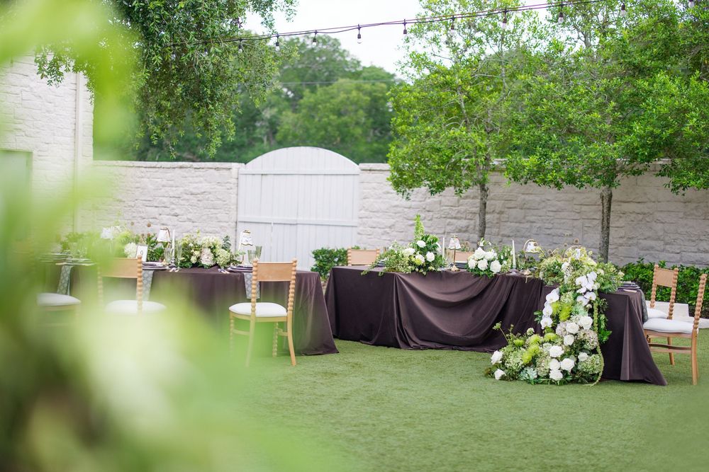 Elegant outdoor wedding reception setup with dark linen sweetheart table, white floral arrangements, and green lawn backdrop.