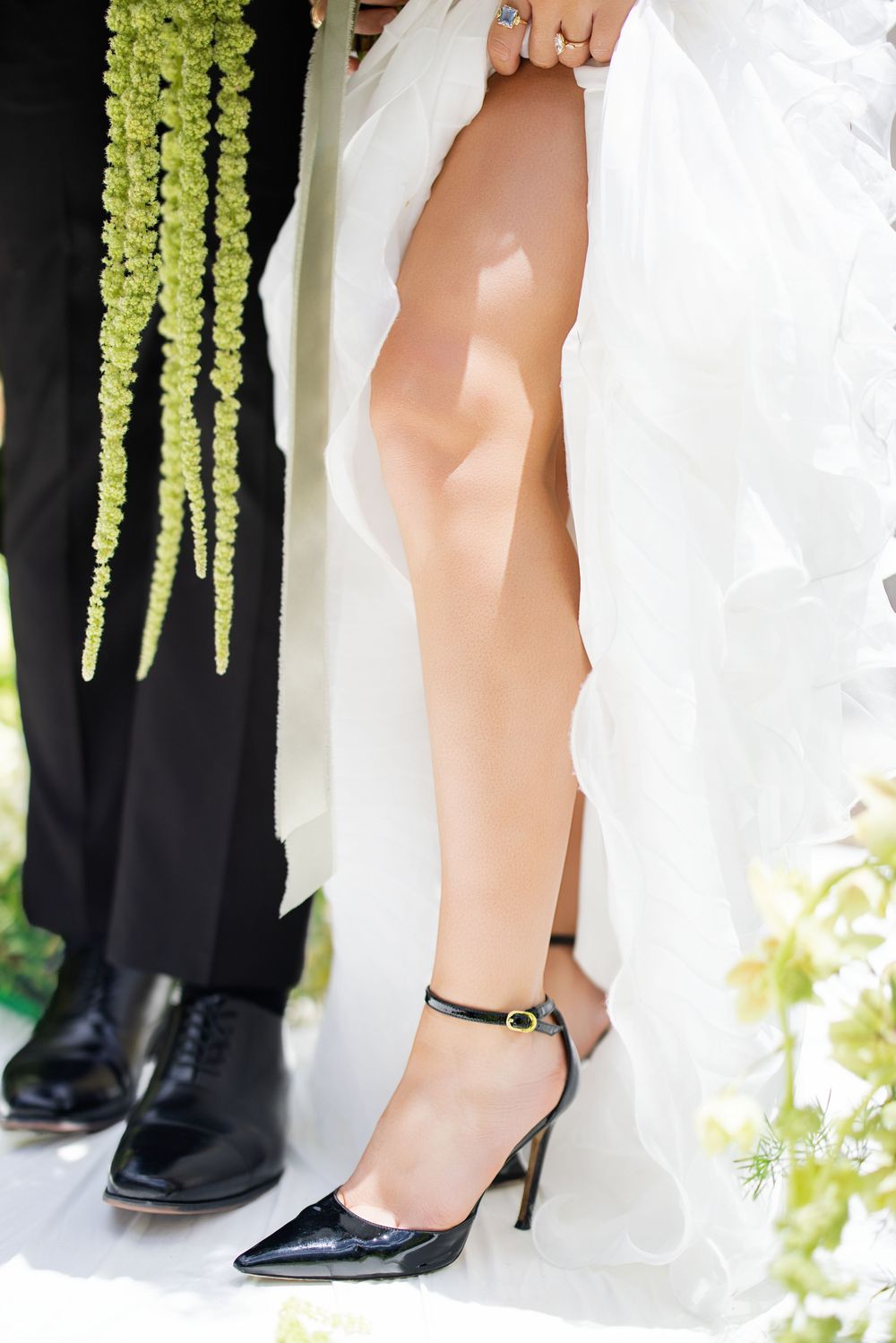 Close-up of bride's legs in black ankle-strap heels beside groom's black oxford shoes at wedding ceremony.