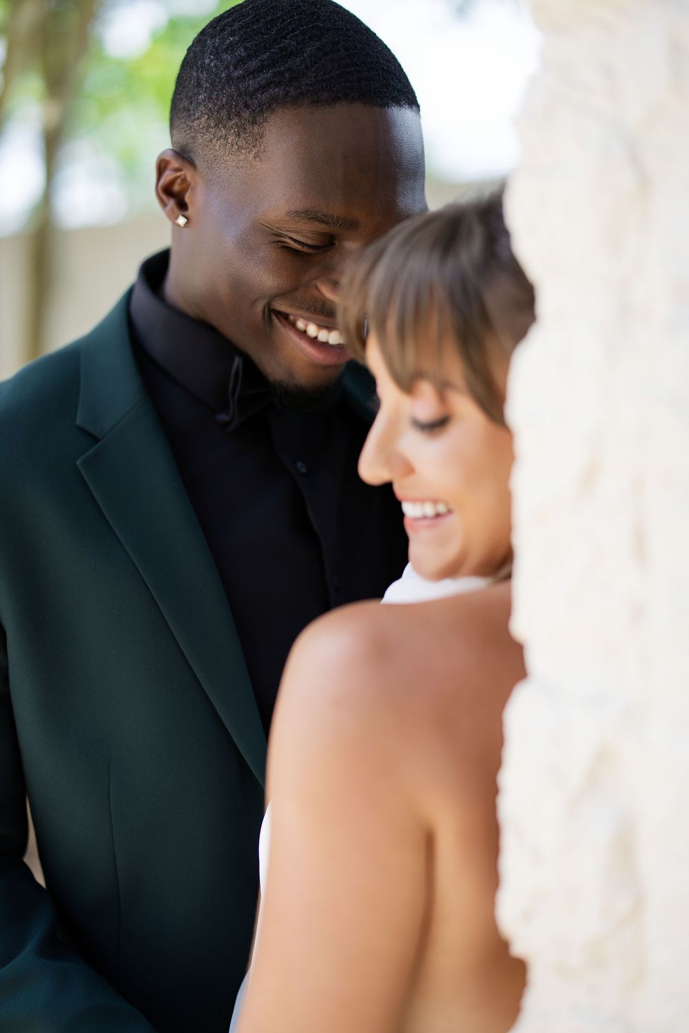 Happy interracial couple sharing a joyful moment, groom in dark suit smiling at bride in white wedding dress.