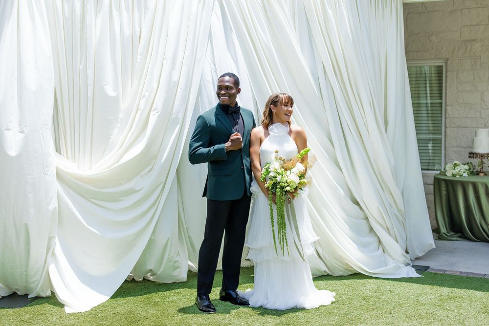 Bride and groom posing together outdoors in front of elegant white draped backdrop on their wedding day.