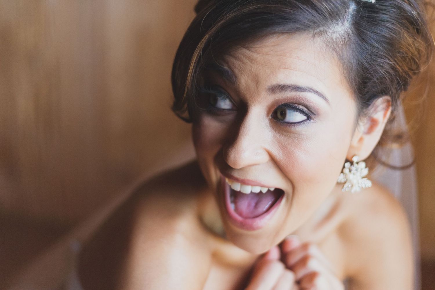 Excited bride with elegant updo and pearl earrings laughing joyfully on her wedding day.