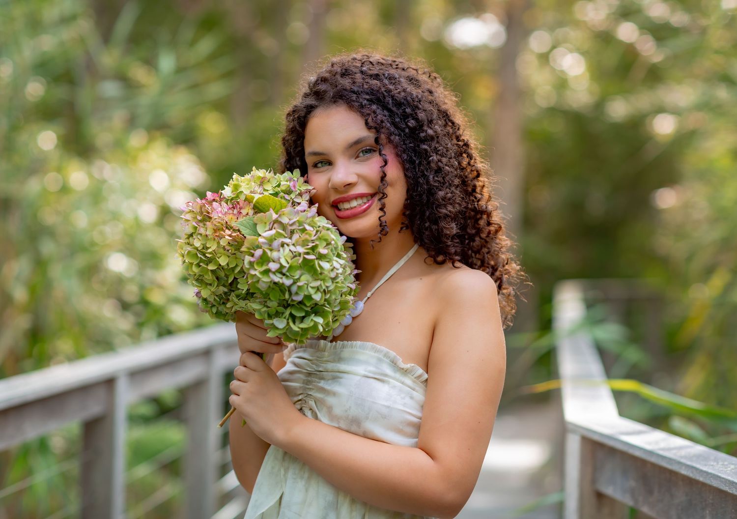 Pregnant woman in gray dress and peach robe poses in golden field by water at sunset.