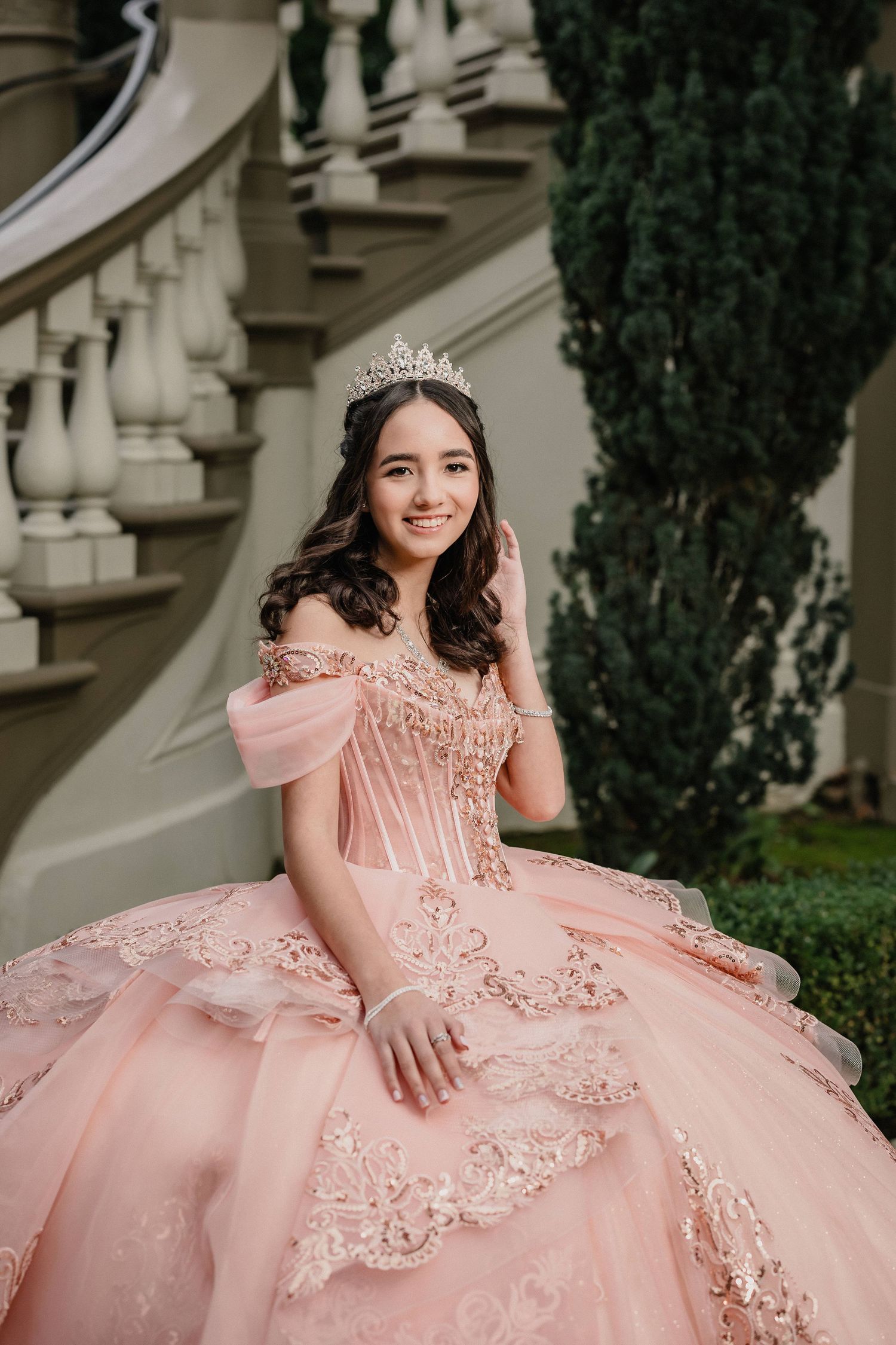 Woman in blue ballgown on ornate gold staircase in elegant mansion with arched windows and chandelier.