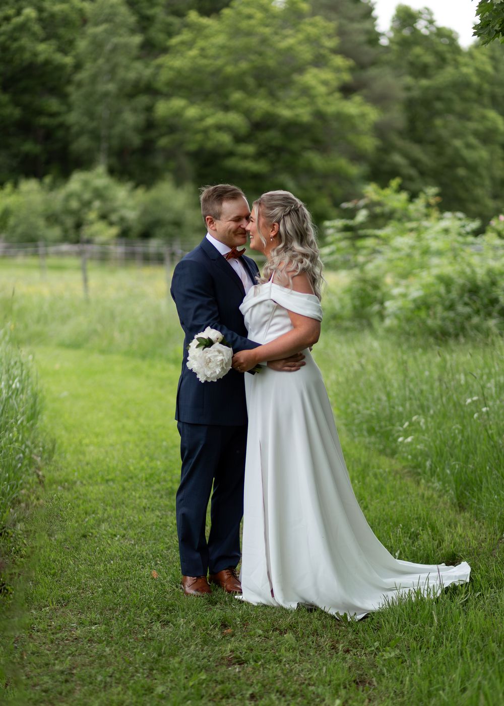 Wedding couple sharing a romantic moment in a green meadow, bride in off-shoulder gown.