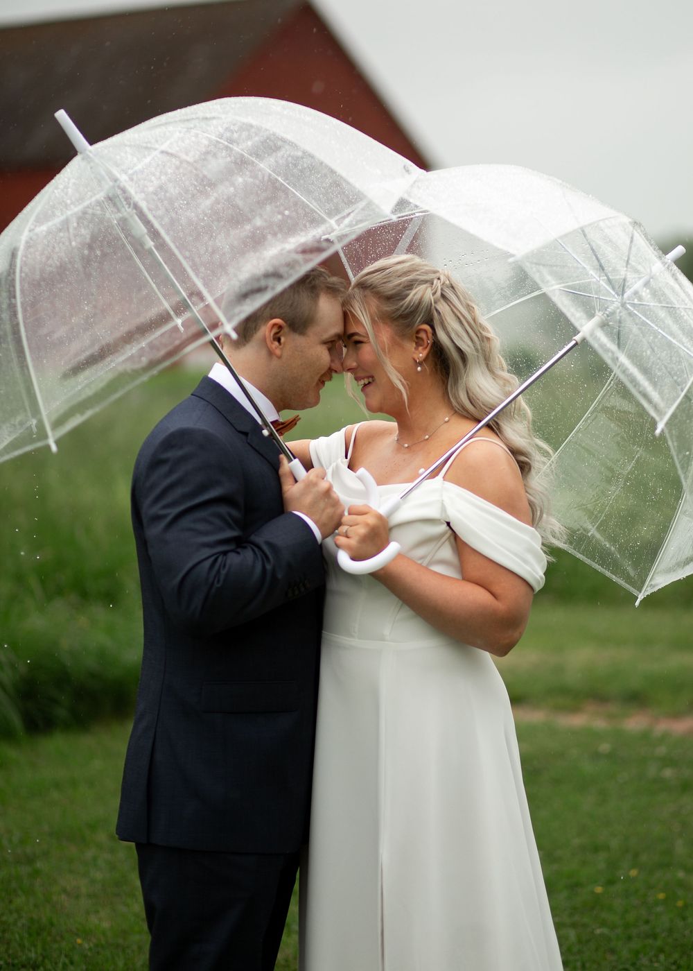 Bride and groom share a romantic moment under a clear bubble umbrella in the rain.