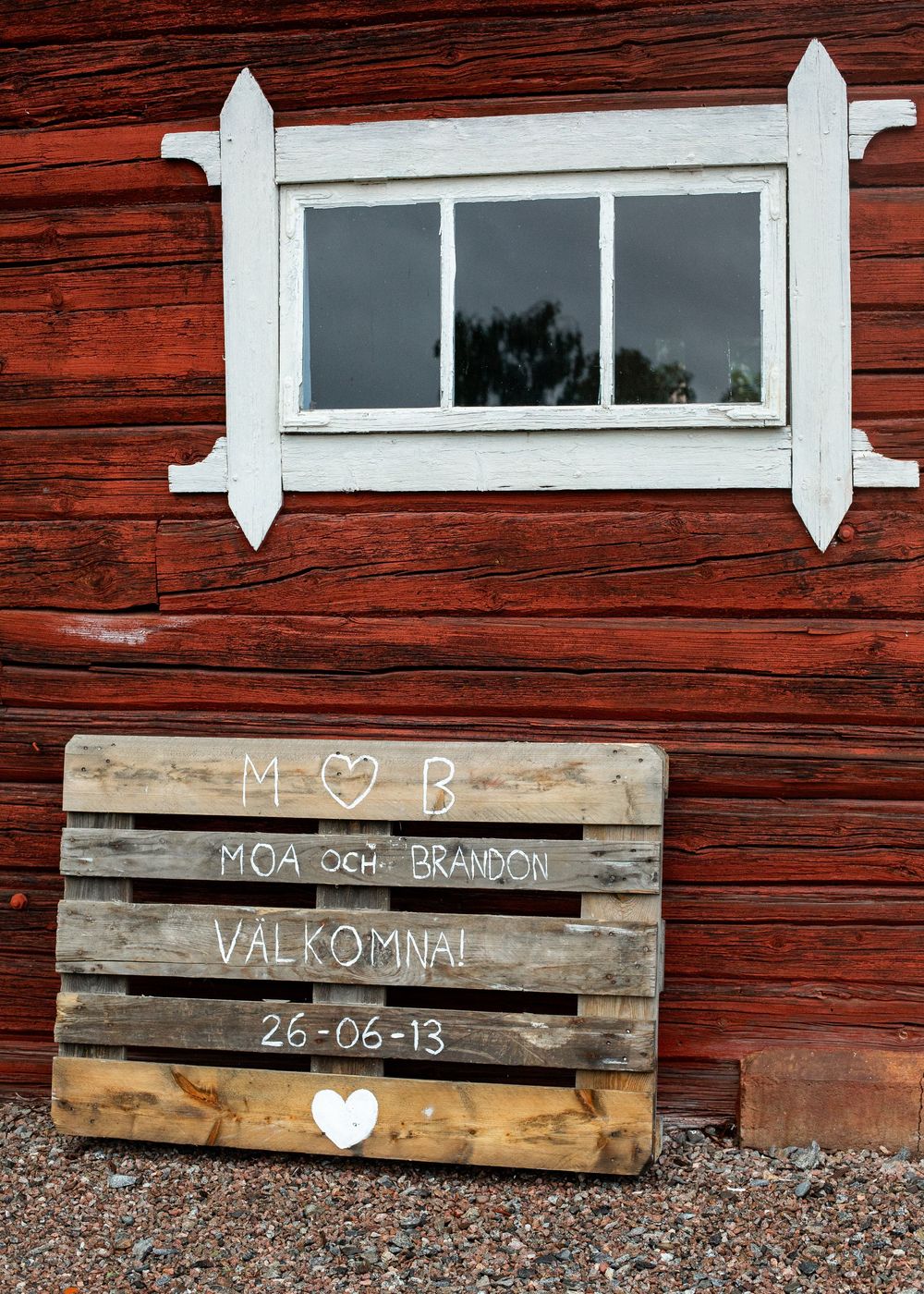 Rustic wooden pallet wedding welcome sign reading Moa och Brandon Valkomna 26-06-13 against red barn wall.