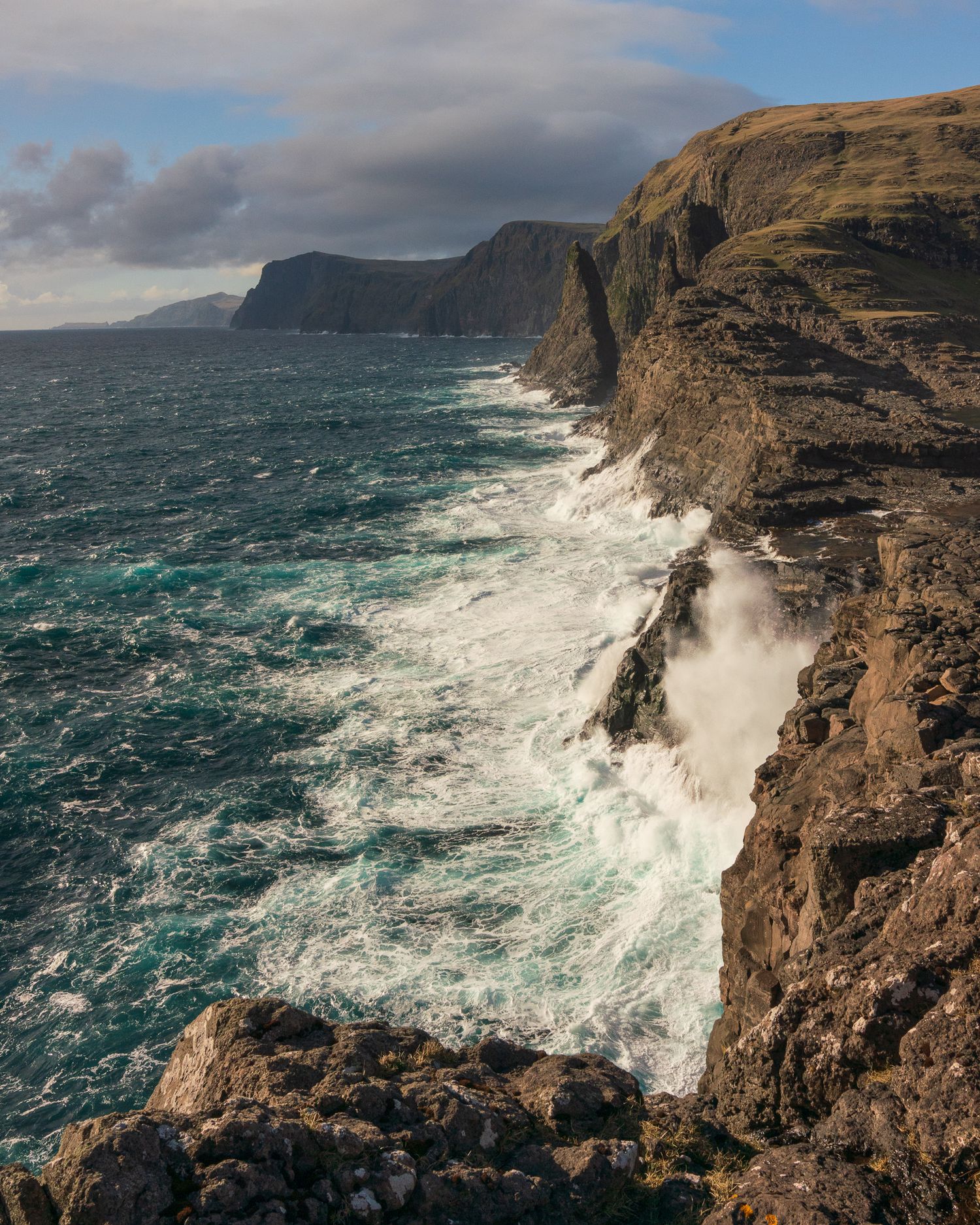 Dramatic Atlantic ocean waves crashing against rugged Faroe Islands coastal cliffs.