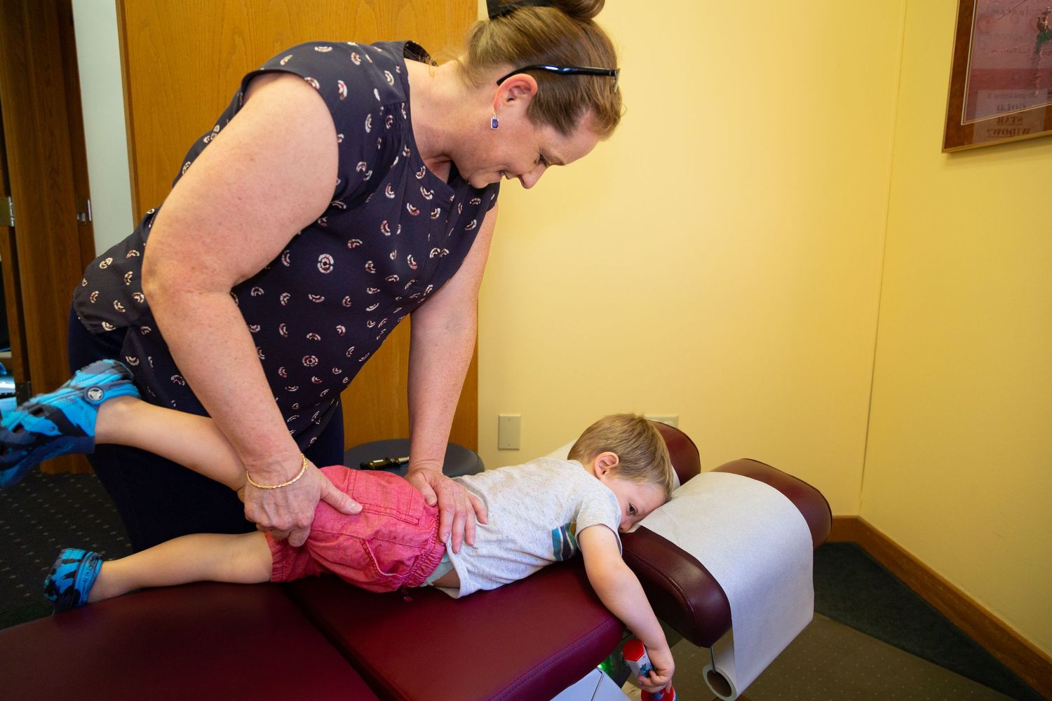 Chiropractor performing gentle spinal adjustment on a toddler lying face-down on a treatment table in a clinic.