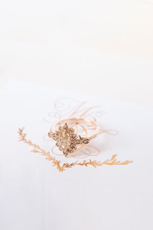 Vintage gold filigree ring with diamond center stone resting on elegant calligraphy stationery with gold botanical accents.