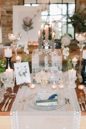 Elegant wedding table setting with candles, floral centerpieces, crystal glassware, and lace runner on a wooden table.