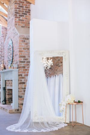 Elegant wedding dress displayed on a ornate white mirror in a rustic venue with exposed brick walls and chandelier.