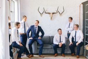 Groomsmen in navy suits and white shirts laughing together in a rustic room with antler wall decor before a wedding.
