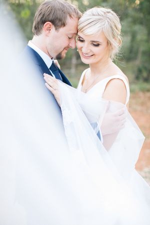Bride and groom share an intimate moment, touching foreheads, bride in white gown, groom in navy suit, soft bokeh background.