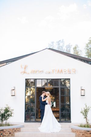 Bride and groom embracing in front of Luce on Timber wedding venue, a modern white barn with large glass doors.