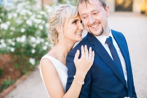 Happy bride and groom sharing a romantic moment outdoors, bride in white dress resting head on groom's shoulder.