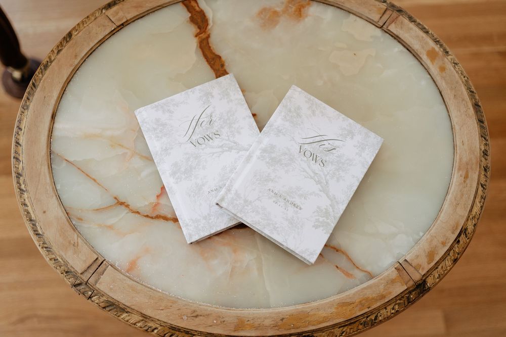 Two elegant marble-patterned wedding vow books displayed on a round onyx marble table.