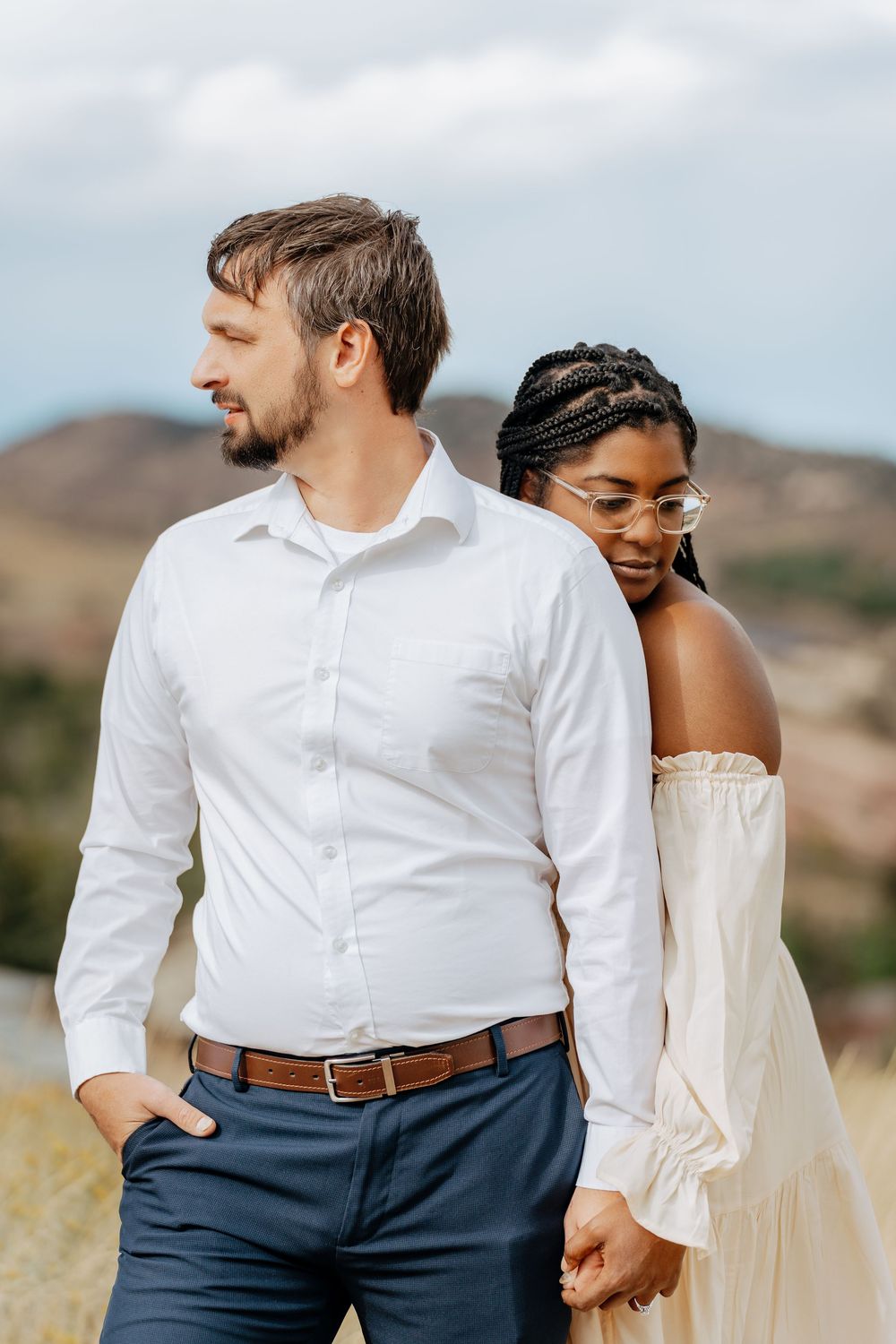 Intimate outdoor couple portrait in white clothing against a mountain landscape.