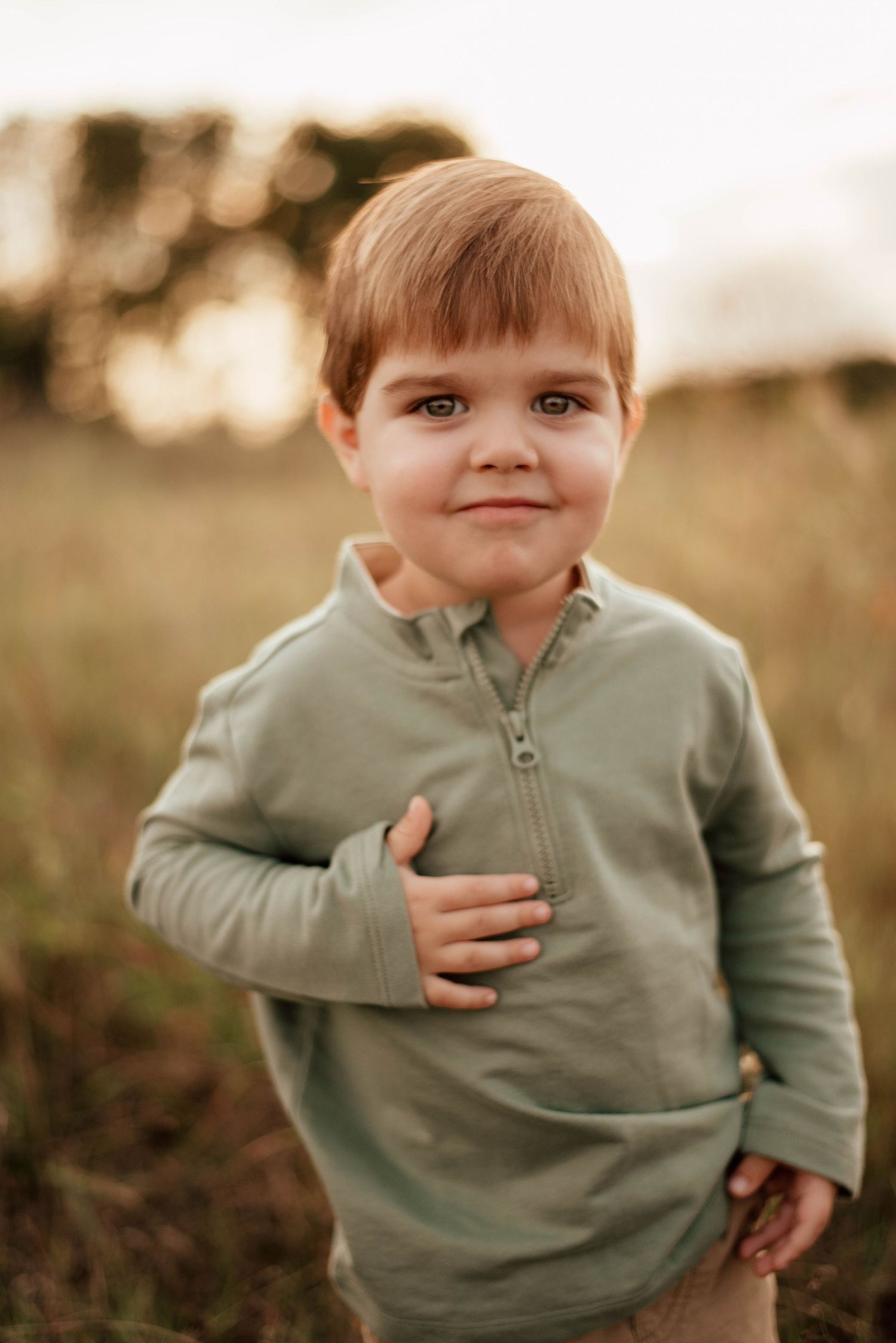 A baby in a blue romper sits on grass during golden hour.