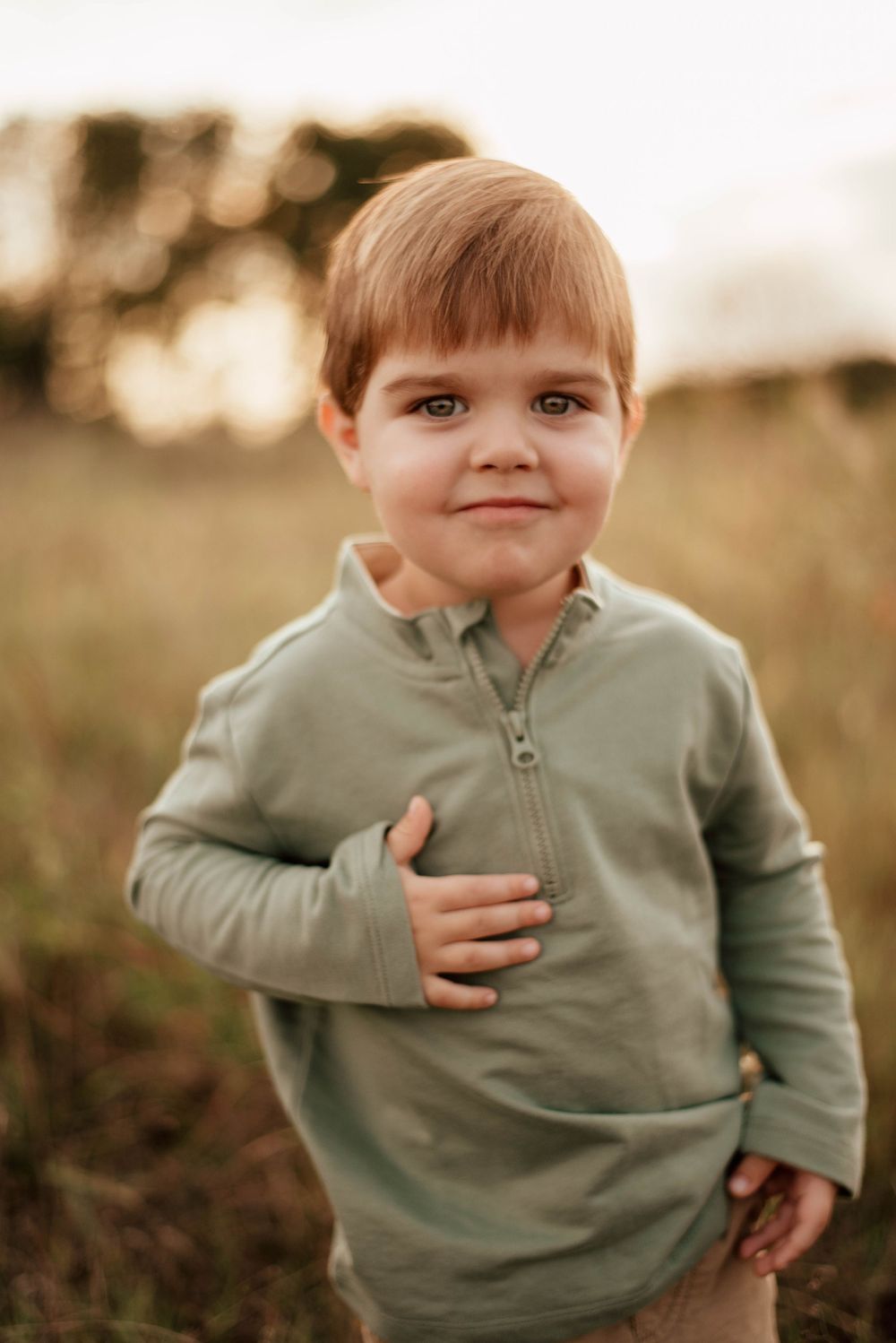 A baby in a blue romper sits on grass during golden hour.