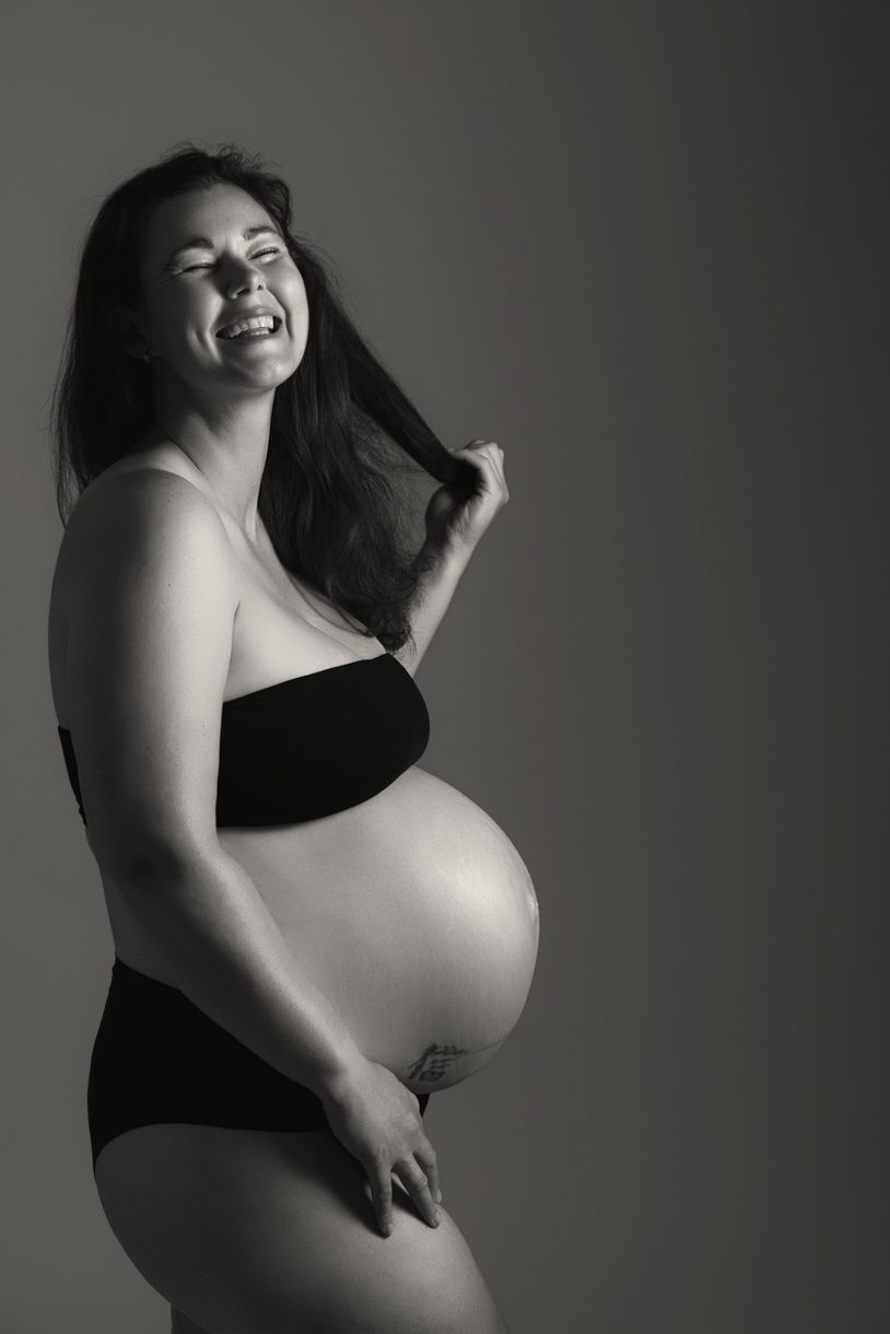 Timeless maternity portrait of a mother-to-be laughing in a North Auckland photography studio.