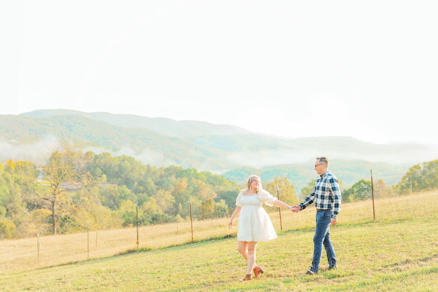 Couple holding hands during a romantic countryside engagement session in Knoxville, Tennessee with scenic mountain views in the background.