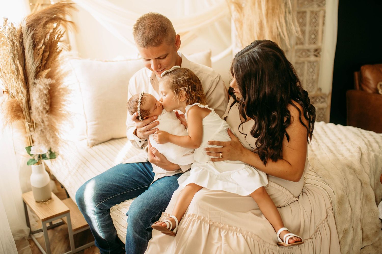 Newborn photography in studio with family of four giving kisses on a bed boho theme studio
