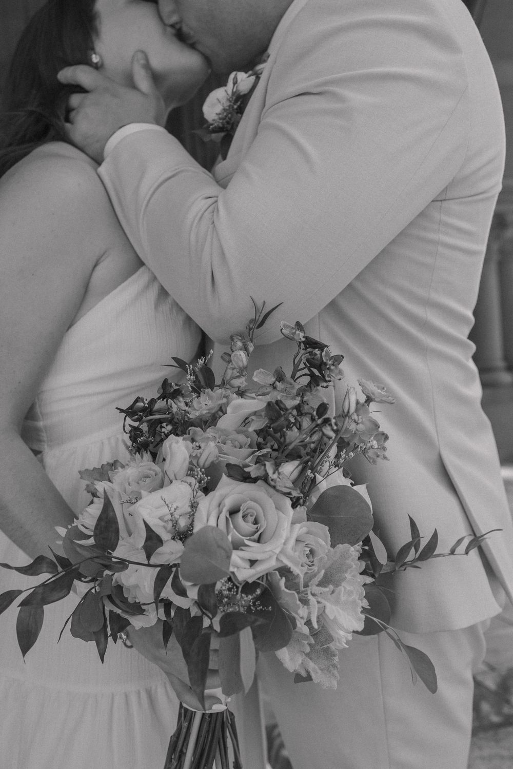 A black and white wedding photo featuring an elegant floral bouquet and embrace.