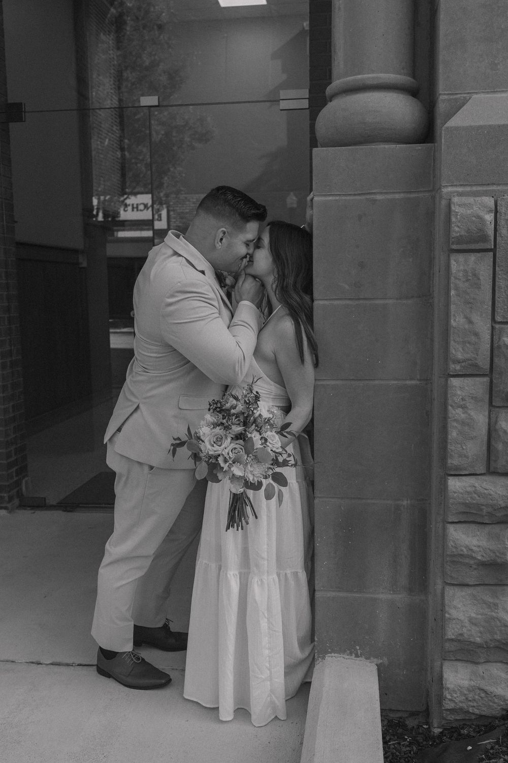 A wedding couple embracing near stone columns in a romantic moment.