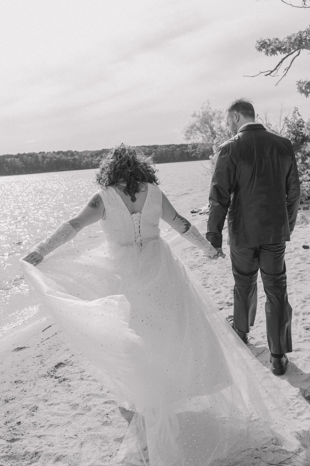 A couple walking along a beach with a flowing white wedding dress catching the breeze.