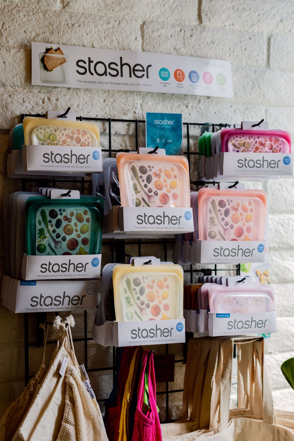 Display of colorful Stasher brand reusable storage bags and containers arranged on wall-mounted retail shelving.