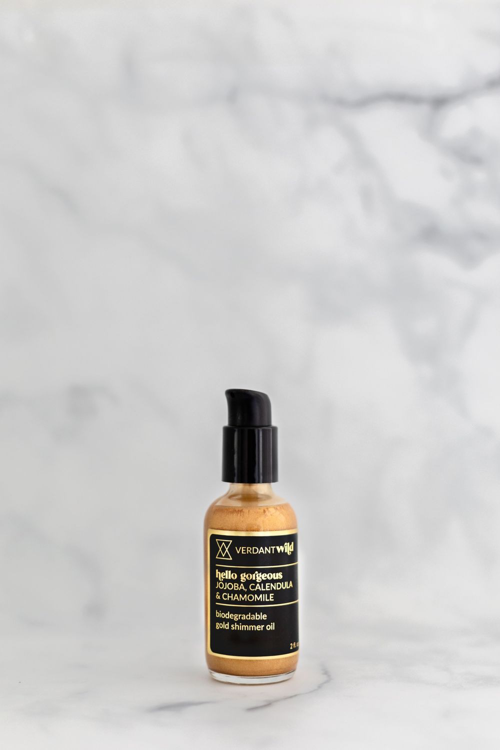 A gold-tinted facial serum bottle with black pump dispenser against a marble backdrop.