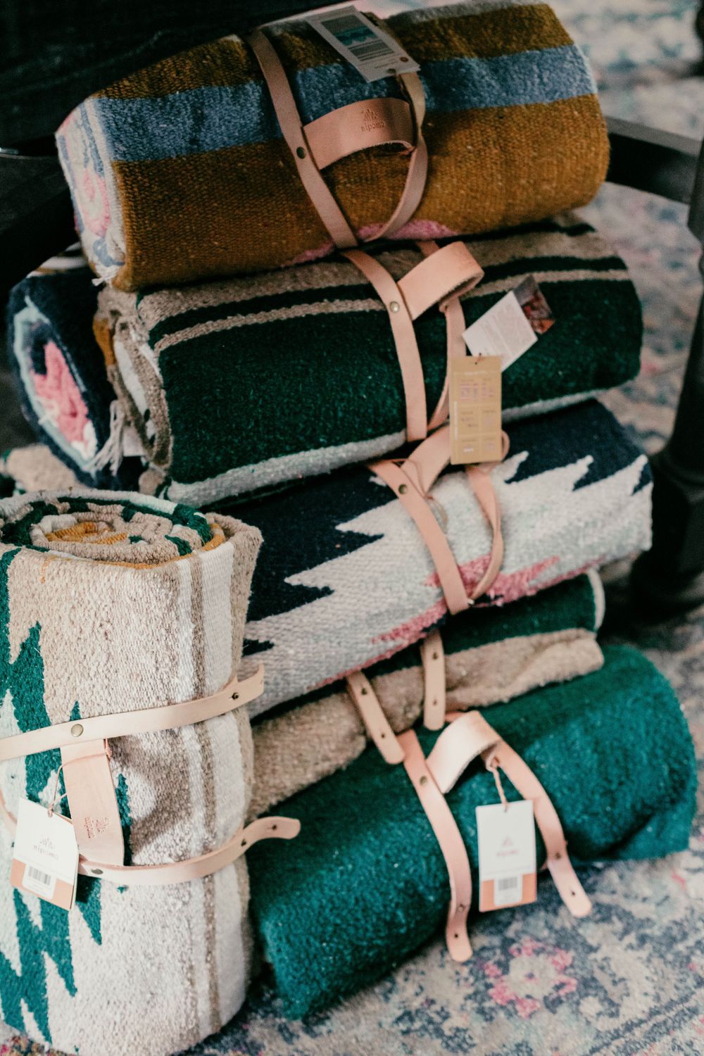 A stack of rolled vintage striped wool blankets bound with leather straps on a patterned surface.