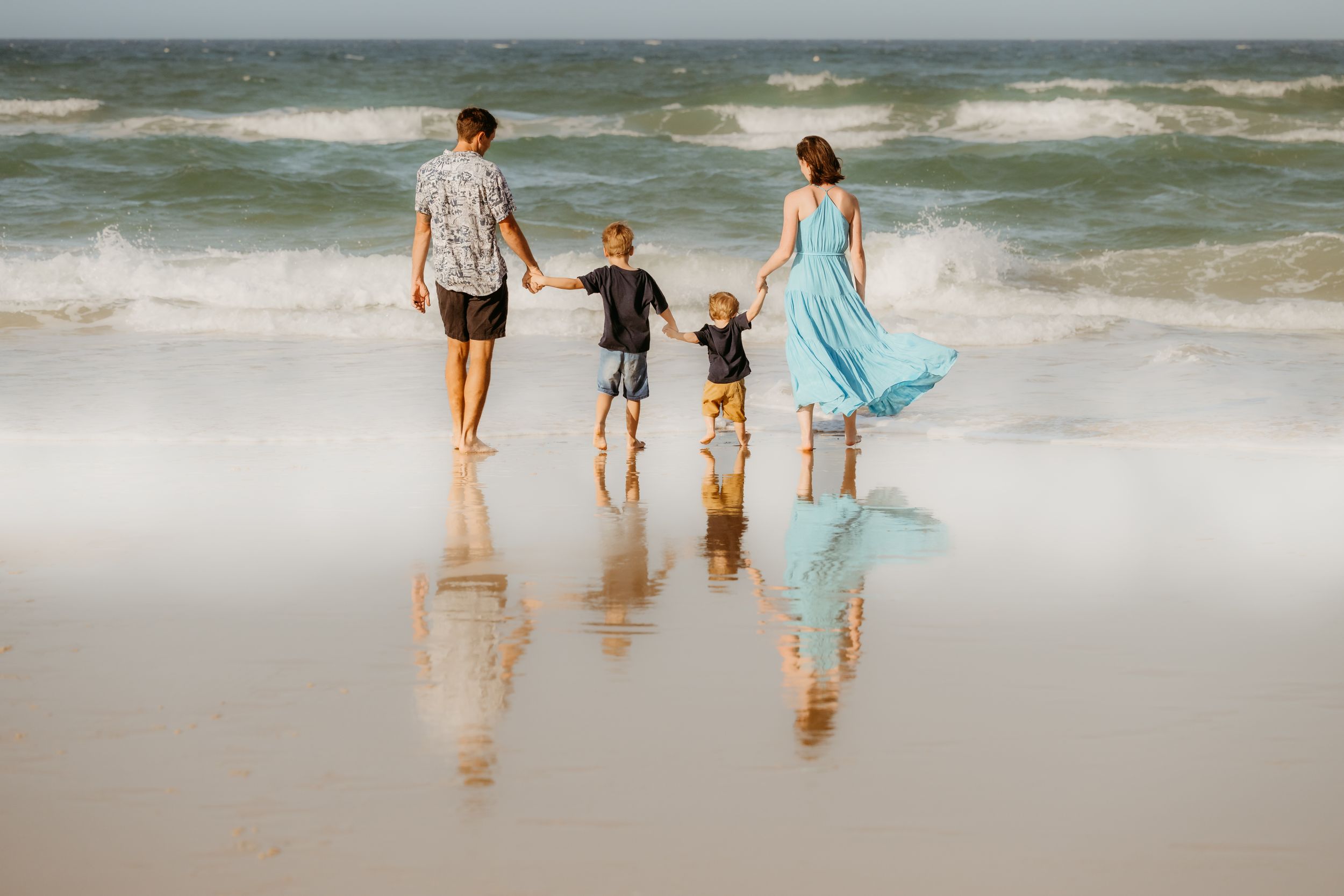 A group walks along a sandy beach with rolling waves and ocean surf in the background.