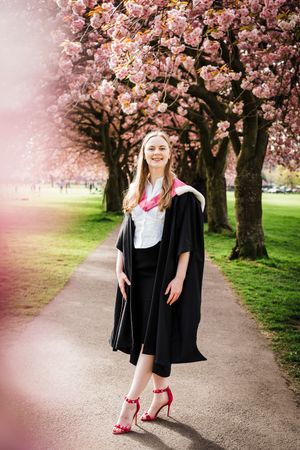 Graduation photography in Edinburgh university, female graduate in cherry blossoms wearing gown and pink high heels.
