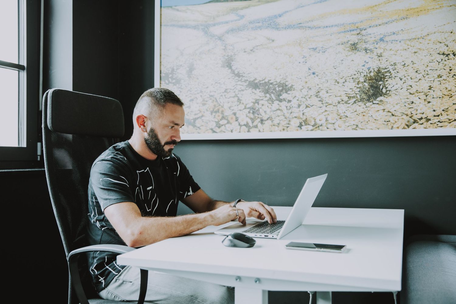 Professional working at white desk with laptop in modern office with landscape art.