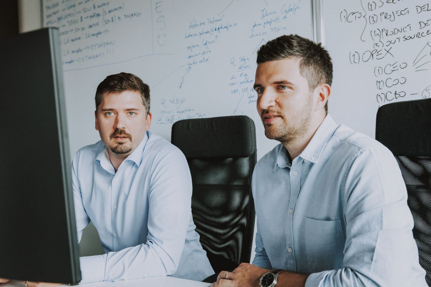 Two professionals in business attire reviewing work at computer station.