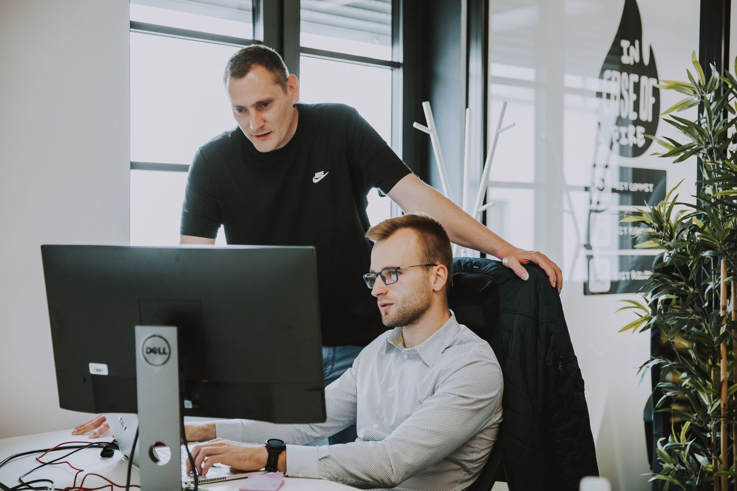 Two colleagues collaborating at computer workstation with indoor plants nearby.