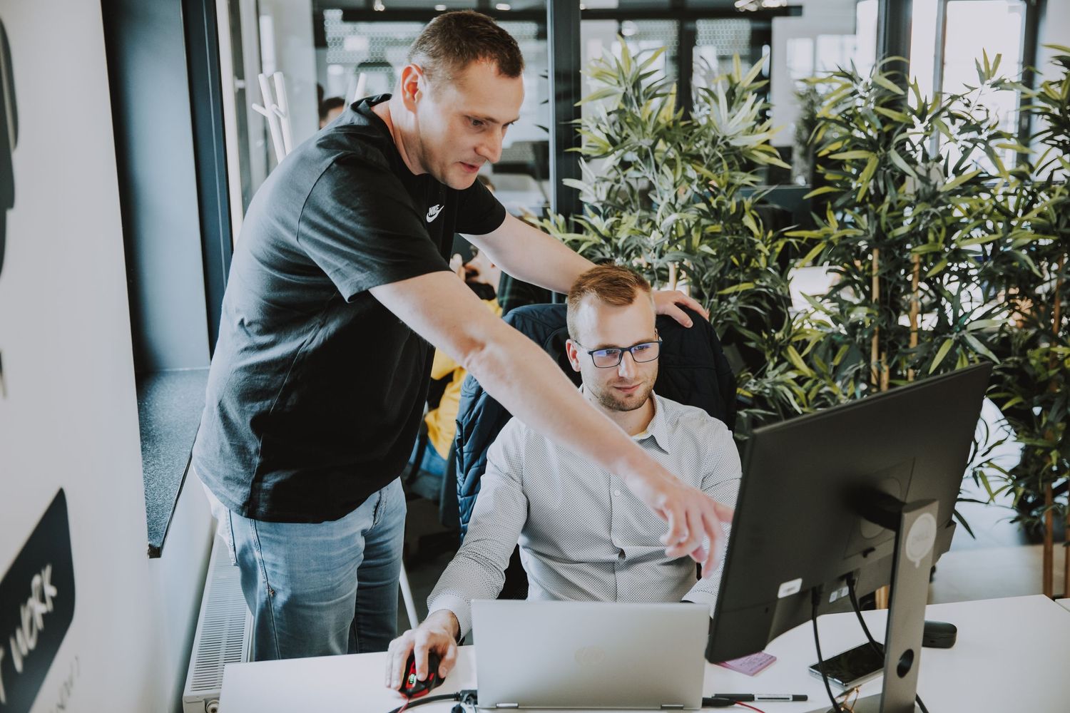 Two team members reviewing work on desktop computer in bright office space.