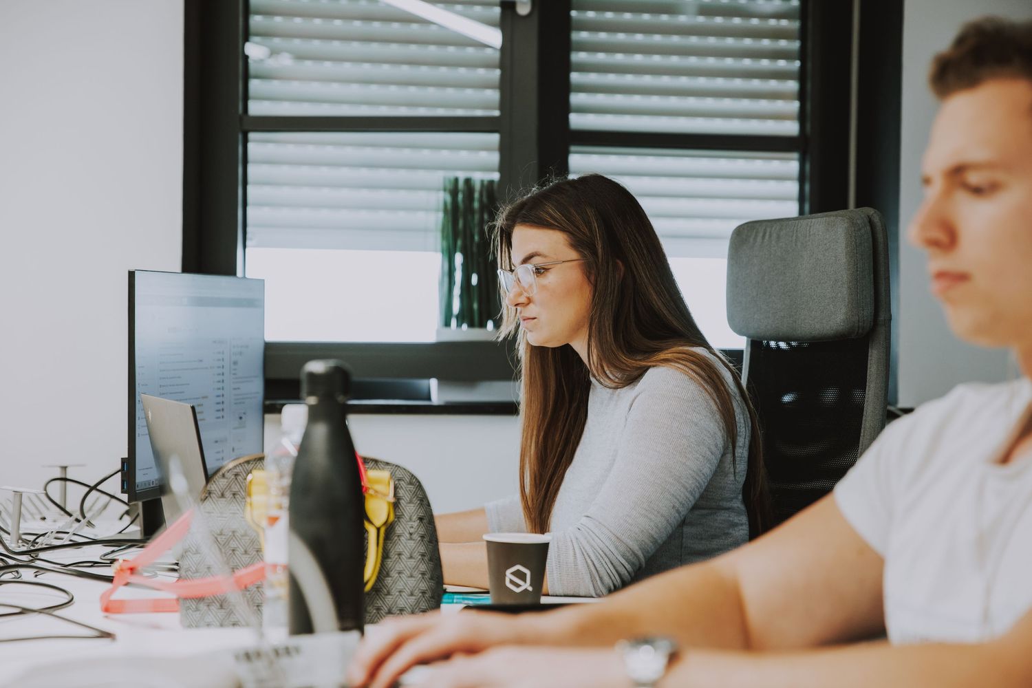 Two professionals working at computer desks in a modern office space.