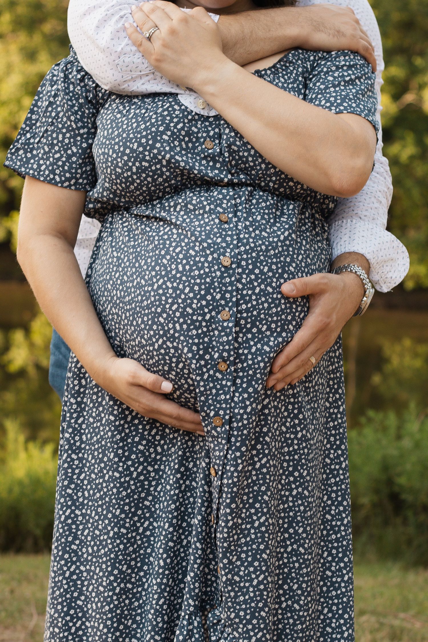 Close up of hands cradling a pregnant belly wearing a blue floral dress.