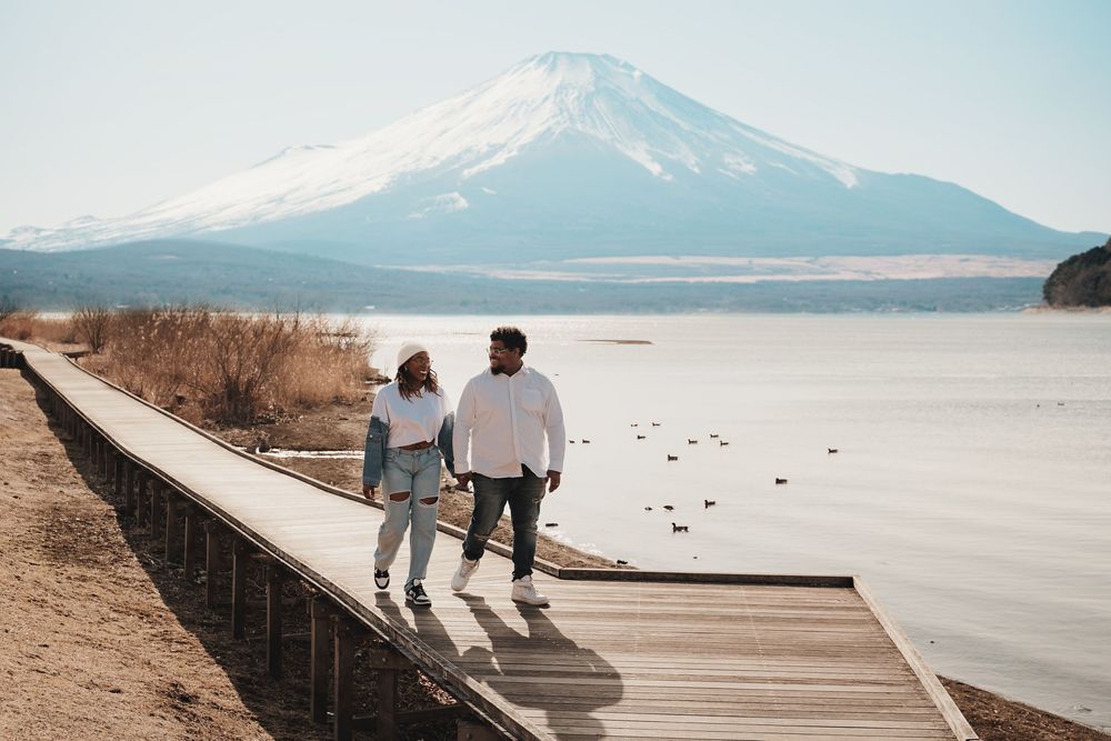 A serene lakeside boardwalk stretches across the dry salt flats with snow-capped mountains in the distance.