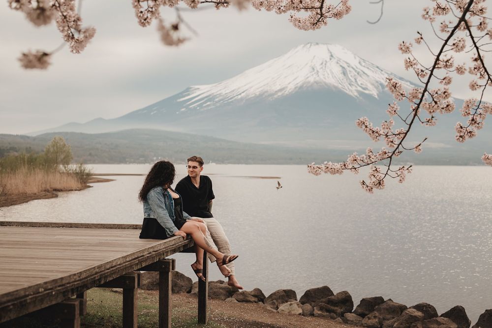 Cherry blossoms frame scenic view of snow-capped Mount Fuji rising above Lake Kawaguchiko in springtime.